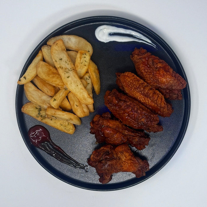 Black plate with steak cut fries and fried wings on a white background. a meal made by Spartan Meal preps a Paramus New Jersey meal prep company.