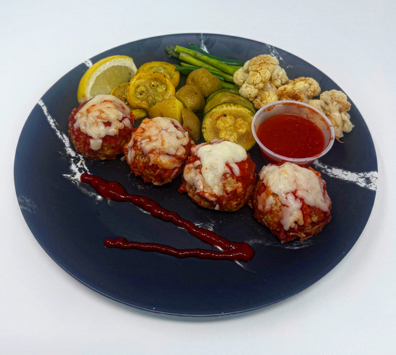 Plated dish with meatballs, vegetables, and a side of sauce on a white background. A low calorie meal made by spartan meal preps.