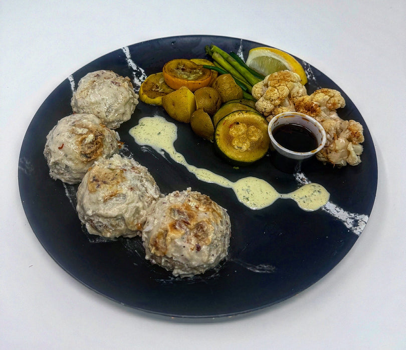 Plated dish with meatballs, vegetables, and a dipping sauce on a white background