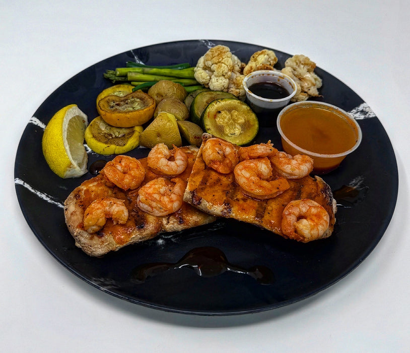 Plated dish with shrimp, bread, vegetables, and sauces on a black plate.