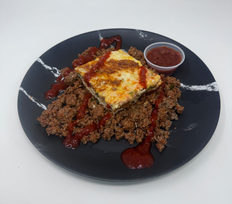 Plated dish with ground meat, omelette, and red sauce on a black plate.
