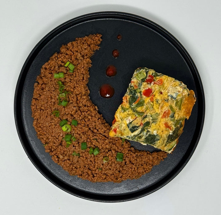 Two dishes on a black plate: one with brown ground meat and green vegetables, the other with a colorful vegetable omelette.