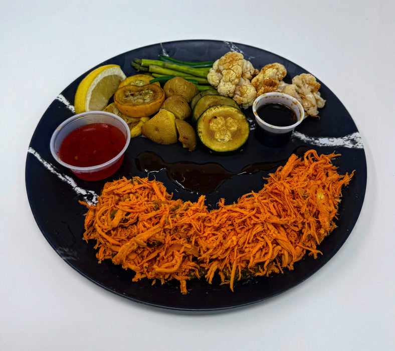 Plated dish with shredded orange food, vegetables, and sauces on a black plate.