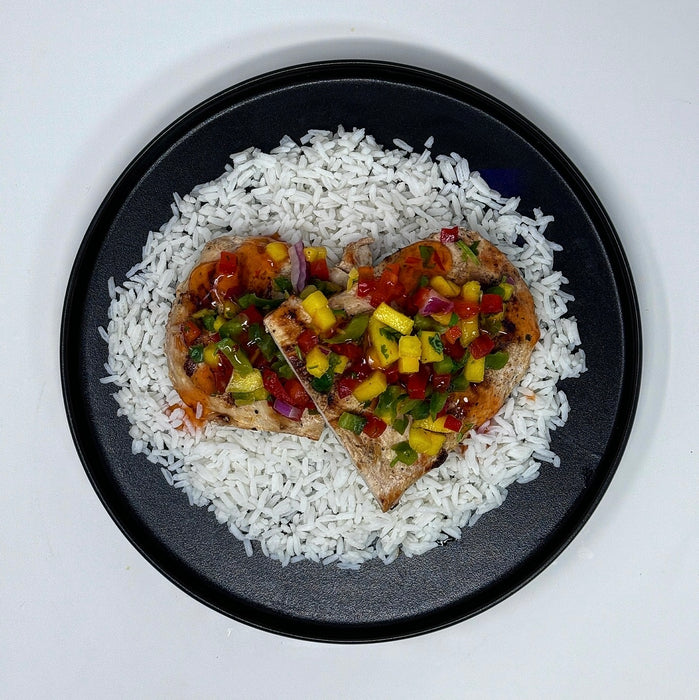 Heart-shaped grilled chicken with pineapple salsa on a bed of rice on a black plate.