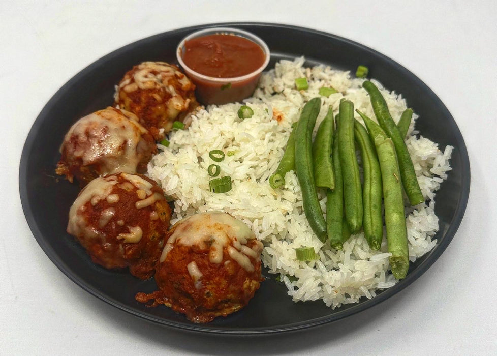 ParmesanChickenMeatballs-SpartanMealPreps-NewJerseyMealPrepDelovery - 4 Parm meatballs served with jasmine rice green beans and a side of sauce cup on a black plate.