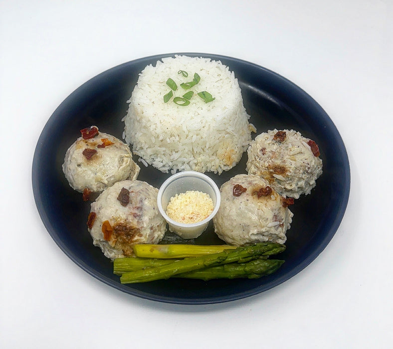 Plated dish with rice, meatballs, and asparagus on a white background