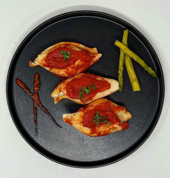 Three pieces of chicken breast with tomato sauce on a black plate with asparagus on a white background
