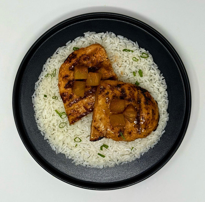 Grilled chicken with pineapple on a bed of rice on a black plate.