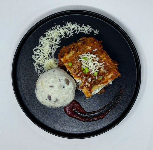 Lasagna with a scoop of mashed potato on a black plate