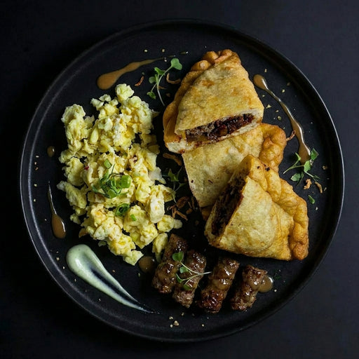 Plated dish with fried empanadas, scrambled eggs, and sausages on a dark background