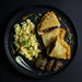 Plated dish with fried empanadas, scrambled eggs, and sausages on a dark background