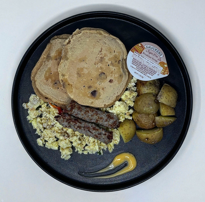 Breakfast plate with pancakes, eggs, sausages, and potatoes on a black plate.