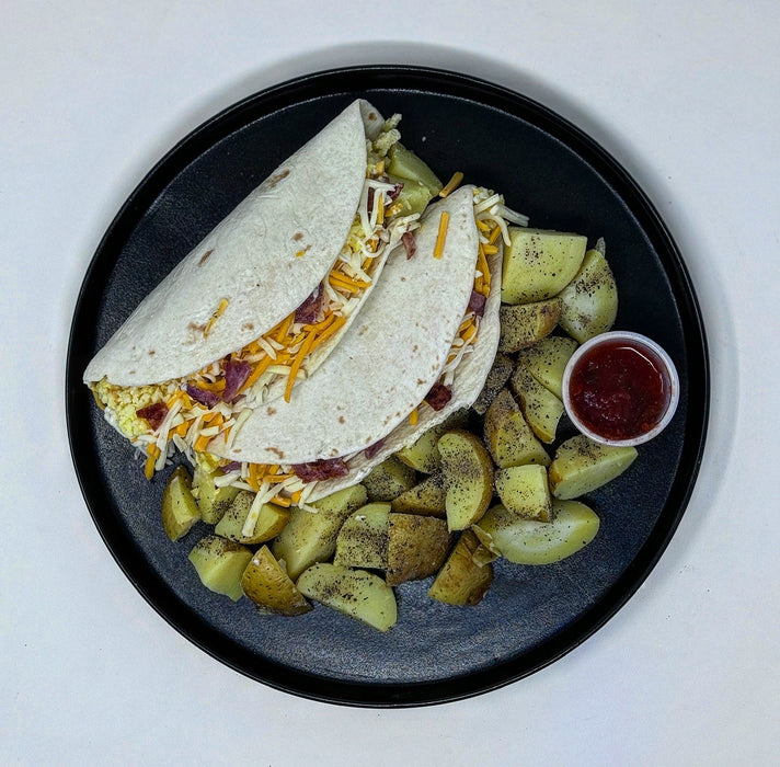 Two tacos with cheese and meat on a plate with potatoes and a side of red sauce.