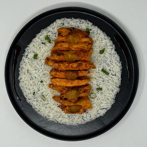 Stack of breaded and fried chicken pieces on a bed of white rice with green herbs in a black bowl.