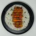 Stack of breaded and fried chicken pieces on a bed of white rice with green herbs in a black bowl.