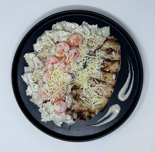 Plated dish with grilled chicken, shrimp, and pasta on a black plate.