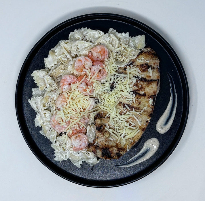 Plated dish with grilled chicken, shrimp, and pasta on a black plate.