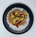 Dish of chicken with vegetables over rice on a black plate