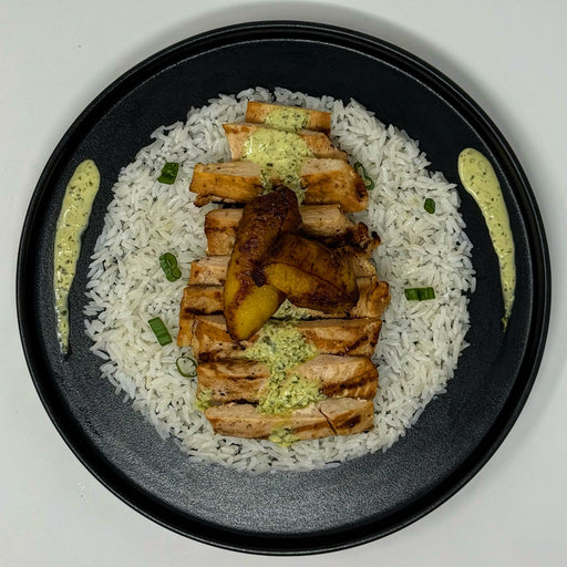 Plated dish with rice, grilled chicken, and vegetables on a black plate.