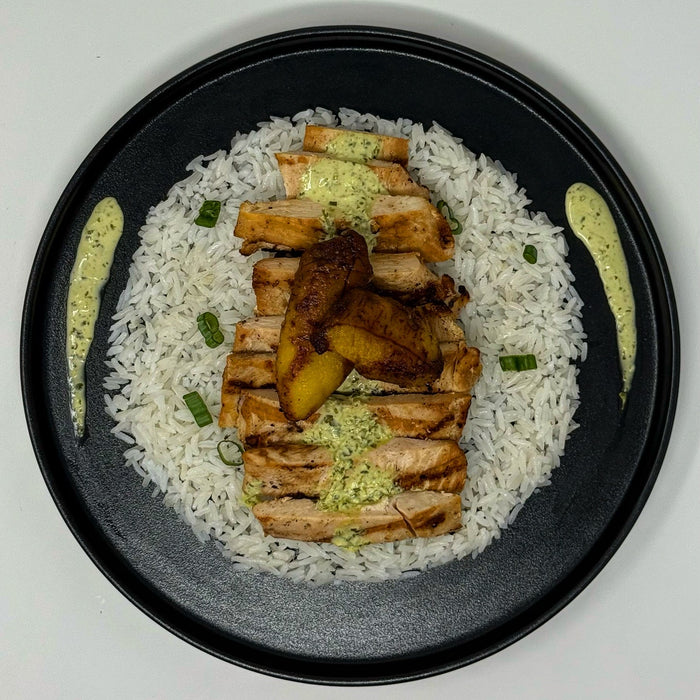 Plated dish with rice, grilled chicken, and vegetables on a black plate.