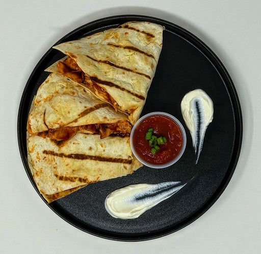 Quesadillas on a black plate with salsa and sour cream on a light gray background