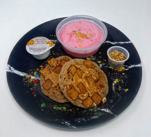 Two cookies with a pink dessert and small container on a black plate with white rim.