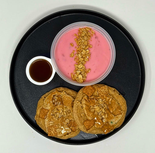 Two pancakes with a side of pink yogurt and granola on a black plate.
