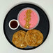 Two pancakes with a side of pink yogurt and granola on a black plate.