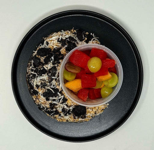 Black plate with a dessert and a container of fruit salad on a white background