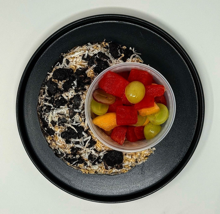 Black plate with a dessert and a container of fruit salad on a white background