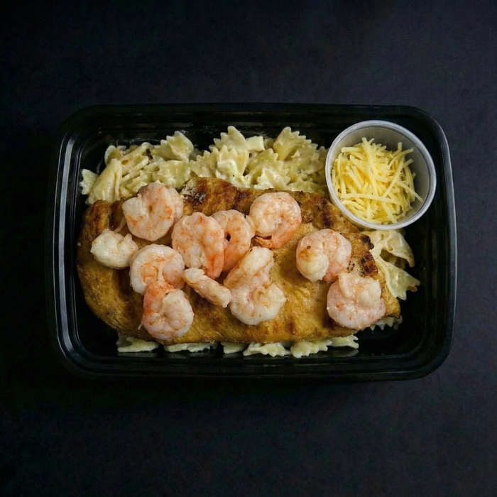Plated dish with shrimp, pasta, and a side of cheese on a dark background