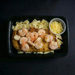 Plated dish with shrimp, pasta, and a side of cheese on a dark background