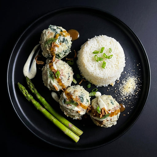 Plated dish with meatballs, rice, and asparagus on a black plate.