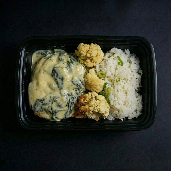 Plated meal with spinach dish, cauliflower, and rice on a dark background
