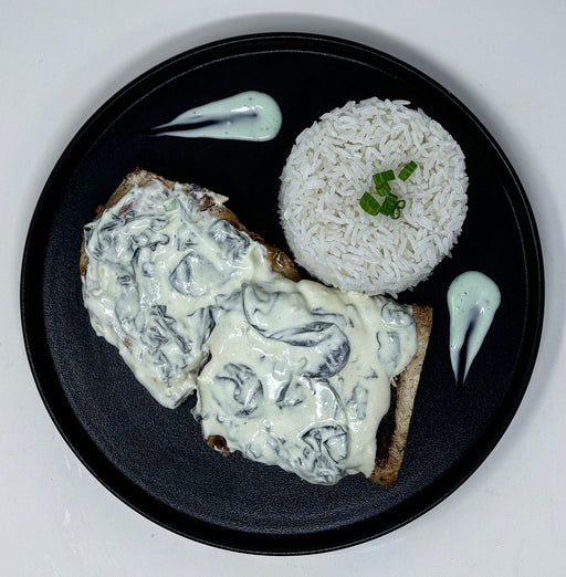 Plated dish of chicken with creamy sauce on a bed of rice, served on a black plate.