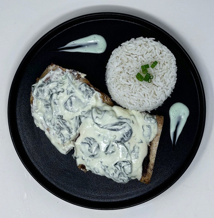 Plated dish of chicken with creamy sauce on a bed of rice, served on a black plate.