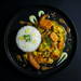 Plated dish with curry, rice, and vegetables on a black background