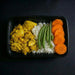 Plated meal with yellow scrambled eggs, white rice, green beans, and orange carrot slices on a black background.