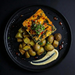 Plated dish with roasted potatoes and a square piece of savory cake on a dark background