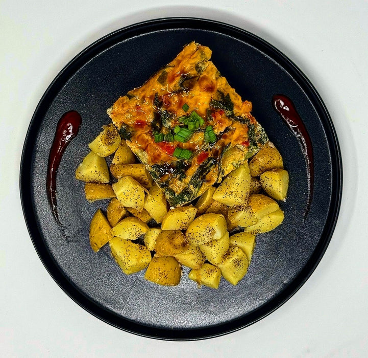 Square piece of vegetable dish on a bed of yellow potatoes with red sauce drizzle on a black plate.