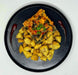 Square piece of vegetable dish on a bed of yellow potatoes with red sauce drizzle on a black plate.