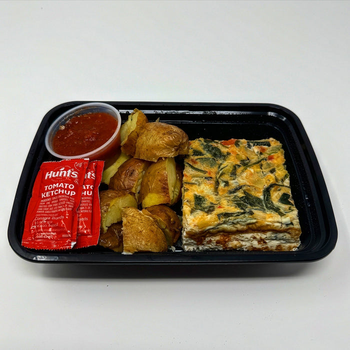 Square piece of vegetable dish on a bed of yellow potatoes with red sauce drizzle on a black plate.