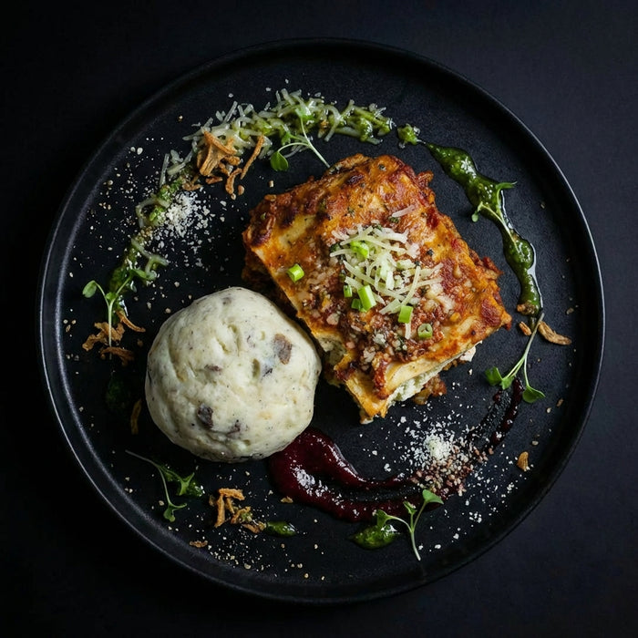 Plated dish with lasagna, garlic bread, and a side of mashed potatoes on a dark background