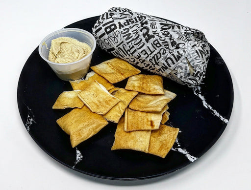 Pita chips on a black plate with hummus and a tortilla wrap on a white background
