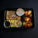 Breakfast meal in a black tray with French toast, fruit, and scrambled eggs on a dark background.
