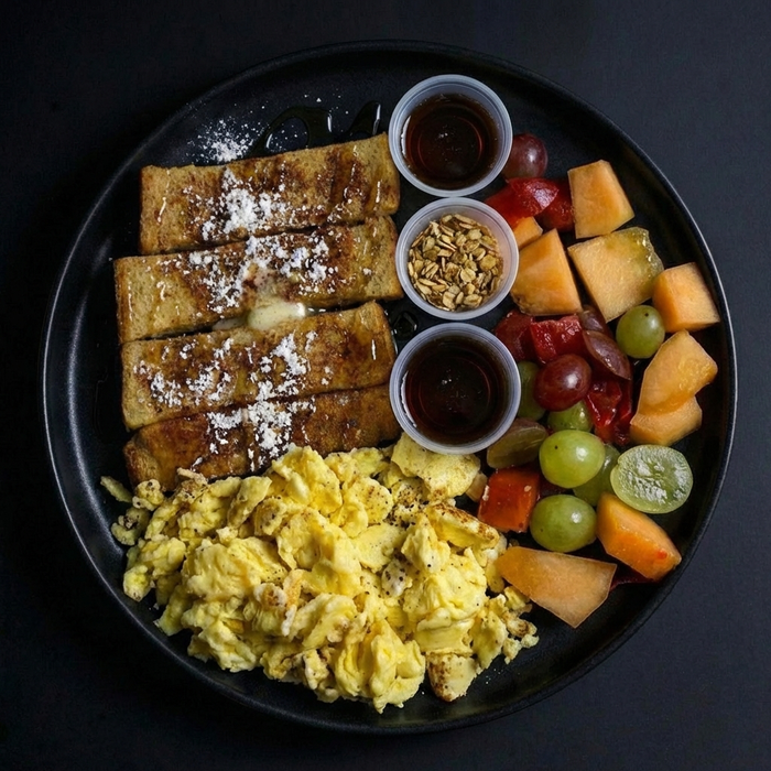 Breakfast plate with French toast, scrambled eggs, and fruit on a black plate.