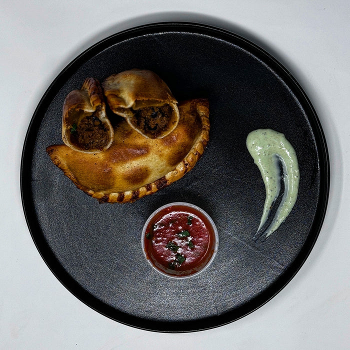 Two empanadas on a dark plate with a side of salsa and guacamole.
