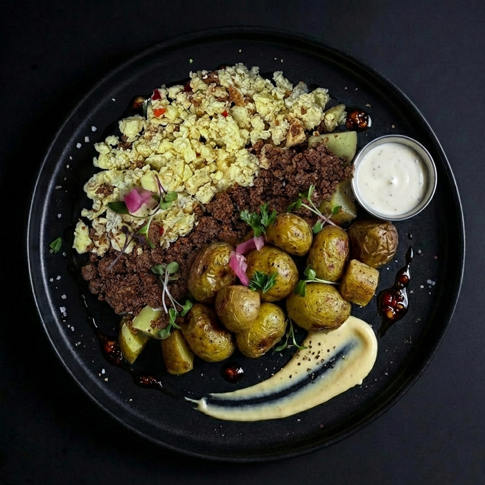 Plated dish with roasted potatoes, quinoa, and a side of sauce on a dark background