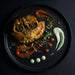 Plated dish with empanadas, sauces, and garnishes on a dark background, a meal made by spartan meal preps.