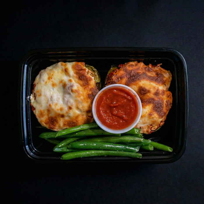 Plated dish with stuffed zucchini boats, green beans, and a side of red sauce on a black background